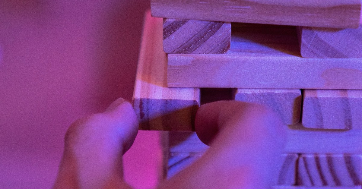 A hand easing a block out of a tower of wooden blocks.
